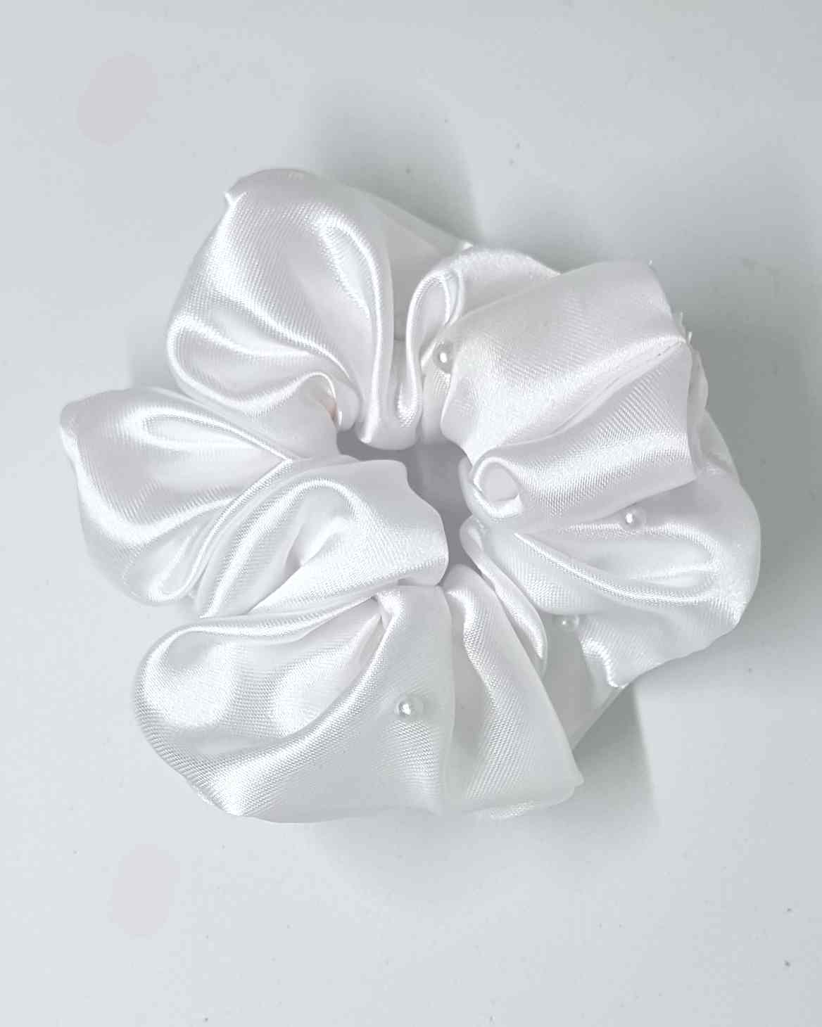 Scrunchie Glam Satin Perlas BlancoEste hermoso scrunchie de satén con perlas es la perfecta combinación para un look femenino y glamuroso. Las perlas son de calidad superior, asegurando detalles duraderos. El scrunchie es hecho a mano, con un tamaño de 12
